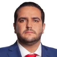 Professional headshot of a man in a dark blue suit and red tie against a white background