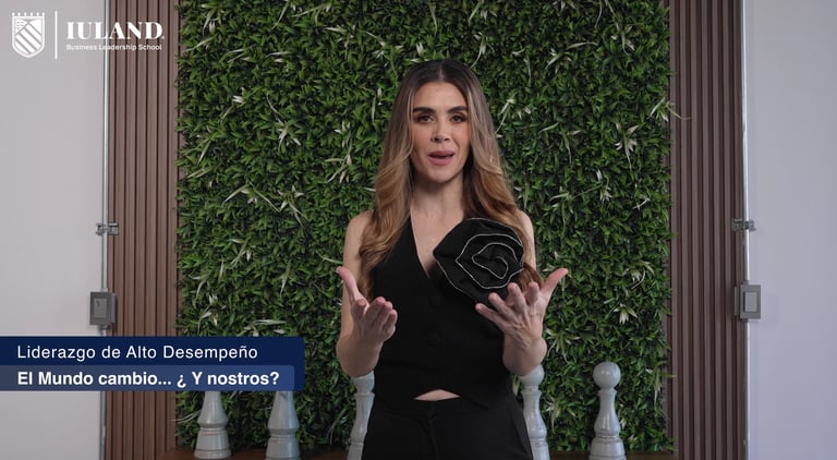 Woman in black blazer speaking in front of green plant wall backdrop with wooden panels and decorative chess pieces