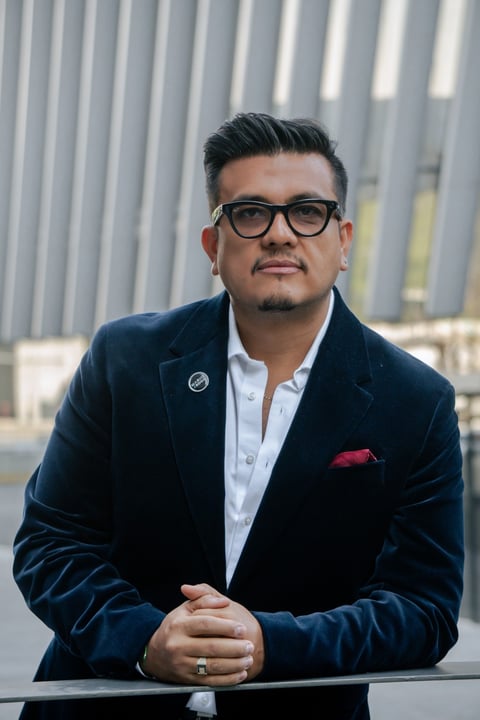 Professional man in navy blazer and glasses posing against striped gray building backdrop
